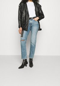 Černá kožená motocyklová bunda se stříbrnými zipy, bílý tričko, světle modré oprané džíny a černé kotníkové boty s špičatou špičkou.