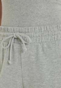 Pantaloni della tuta grigi con un tessuto testurizzato, dotati di vita elasticizzata e cordoncino per la regolazione. Design semplice, senza motivi.