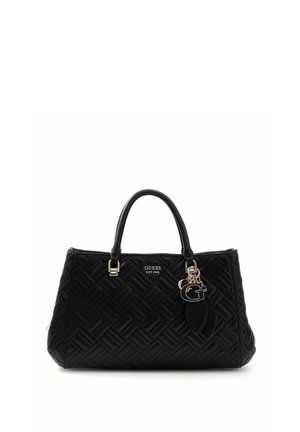 Sac à main noir matelassé avec double poignée, logo GUESS et charm métallique décoratif en forme de "G" et de feuille.