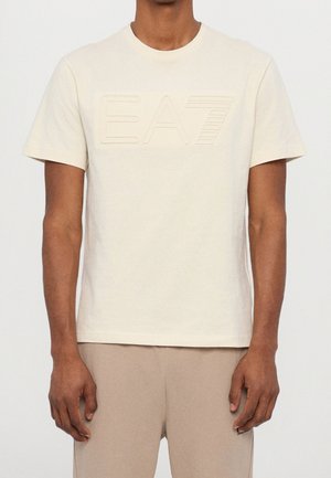 Cremefarvet bomulds-t-shirt med korte ærmer, med en fremhævet EA7-logo på forsiden. T-shirten har rund halsudskæring og en afslappet pasform.