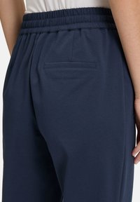 Marine joggers met een elastische tailleband en een enkele achterzak. Gladde stoftextuur met een ontspannen pasvorm, ontworpen voor comfort.