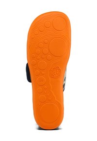 Semelle orange vif d’une chaussure d’enfant avec des motifs circulaires, marquage taille 28 et un petit visage d’animal en relief près de la zone de la voûte plantaire.