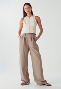Top attillato in ecopelle crema con zip anteriore, abbinato a pantaloni beige chiaro a vita alta e sandali neri.