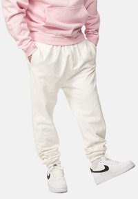 Weiße Baumwoll-Jogginghosen mit elastischem Bund und Bündchen, kombiniert mit weißen Turnschuhen mit schwarzem Nike-Swoosh. Hellrosa Kapuzenpullover.