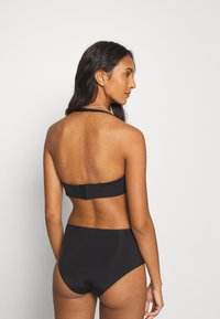Črn bikini komplet, ki vključuje brezramni top z zaponko in visoko pas široke hlačke, gladka tekstura z minimalističnim dizajnom.