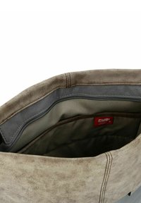 Bruine leren tas interieur met zachte grijze voering, bovenste ritsluiting en een klein rood label. Soepele textuur met subtiele nerfdetails.