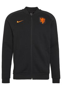 Zwarte zip-up jas van zachte stof. Beschikt over een oranje Nike-logo op de borst en een leeuwenembleem. Inclusief twee zijzakken.