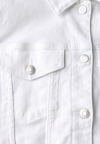 Biała dżinsowa kurtka z srebrnymi zatrzaskami, klasycznym kołnierzykiem, dwiema kieszeniami na piersi oraz delikatnymi liniami tekstury na materiale.