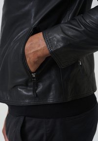 Zwarte leren jas met een ritzak en geribde trui-mouwen. Gladde textuur met een slim-fit ontwerp en gestructureerde kraag.