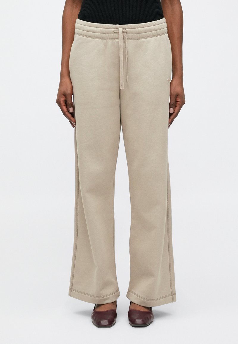 Béžové tepláky vyrobené z mäkkej látky, so elastickým pásom so šnúrkou, širokými nohavicami a viditeľnými švami.