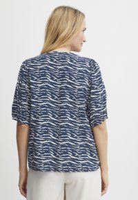 Top corto navy con maniche a sbuffo, caratterizzato da un motivo ondulato bianco, scollo rotondo e un tessuto morbido. Vestibilità morbida.