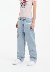 Light blue baggy jeans with embroidered graphic design, featuring a skull and colorful accents. Paired with a pink fitted t-shirt.
