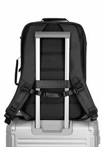 Schwarzer Stoffrucksack mit gepolstertem Rücken und Trägern, ausgestattet mit einem integrierten silbernen Aluminium-Trolleygriff, der sicher an einem silbernen Koffer befestigt ist.