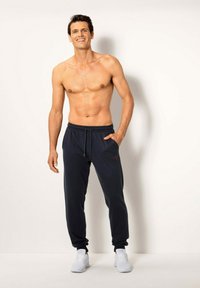 Dunkelblaue, leichte Jogginghosen mit einem elastischen Bund, Kordelzug, Seitentaschen und dezentem roten Logodetail. Weiße Sneaker runden den Look ab.