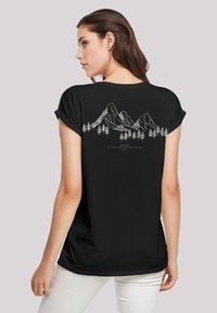 Zwarte shirt met opgerolde mouwen en een witte bergen- en bomenlijn grafiek op de achterkant. Zacht materiaal en een ontspannen pasvorm.