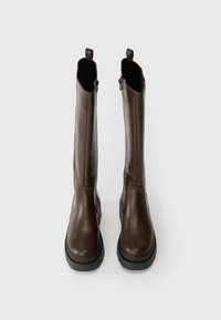 Bruna läderknähöga stövlar med matt yta, robust svart gummisula och dragflikar upptill för enkel påtagning.