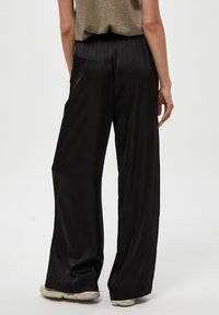 Svarta satinbyxor med vida ben, en slät yta, elastisk midja och flödande silhuett, tillsammans med en metallisk topp.