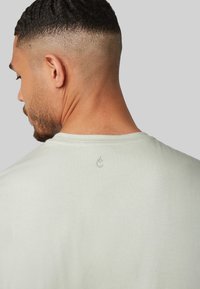 Lichtgroen t-shirt gemaakt van zachte stof, met een ronde hals en een klein waterdruppel logo geborduurd op de achterkant.