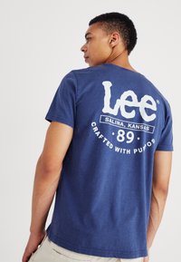 Granatowa bawełniana koszulka z okrągłym dekoltem, krótkimi rękawami i dużym białym logo graficznym na plecach, które zawiera tekst oraz okrągły wzór.