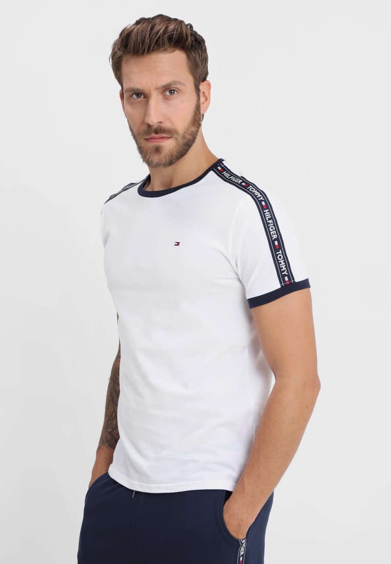Weißes Baumwoll-T-Shirt mit navyblauem Kragen und Ärmelbündchen, versehen mit einem markierten Band entlang der Schultern und einem kleinen Logo auf der Brust.
