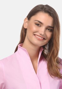 Blusa collared rosa chiaro con una texture liscia, dotata di un colletto rigido e linee pulite, adatta per un abbigliamento casual o formale.