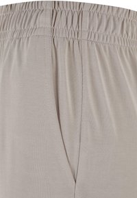Pantalon à taille élastique beige clair avec coutures visibles et détail de poche latérale en tissu doux et lisse.