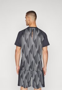 Short-sleeve athletic shirt with a black and white striped pattern, featuring orange detailing, and paired with matching shorts.