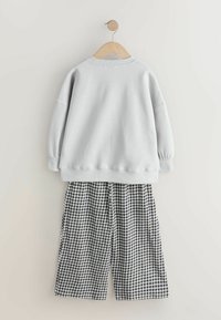 Sweat-shirt gris clair avec épaules tombantes et poignets côtelés suspendu au-dessus d'un pantalon large à carreaux noir et blanc. Texture lisse.