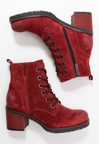 Rote Wildlederschuhe bis zu den Knöcheln mit strukturiertem Finish, schwarzen Schnürsenkeln und einem seitlichen Reißverschluss. Großer Absatz und Gummisohle für besseren Halt.