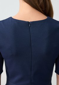 Navyblauwe jurk met een ronde hals en korte mouwen, voorzien van een ritssluiting aan de achterkant en een aansluitende pasvorm met een gladde stofstructuur.