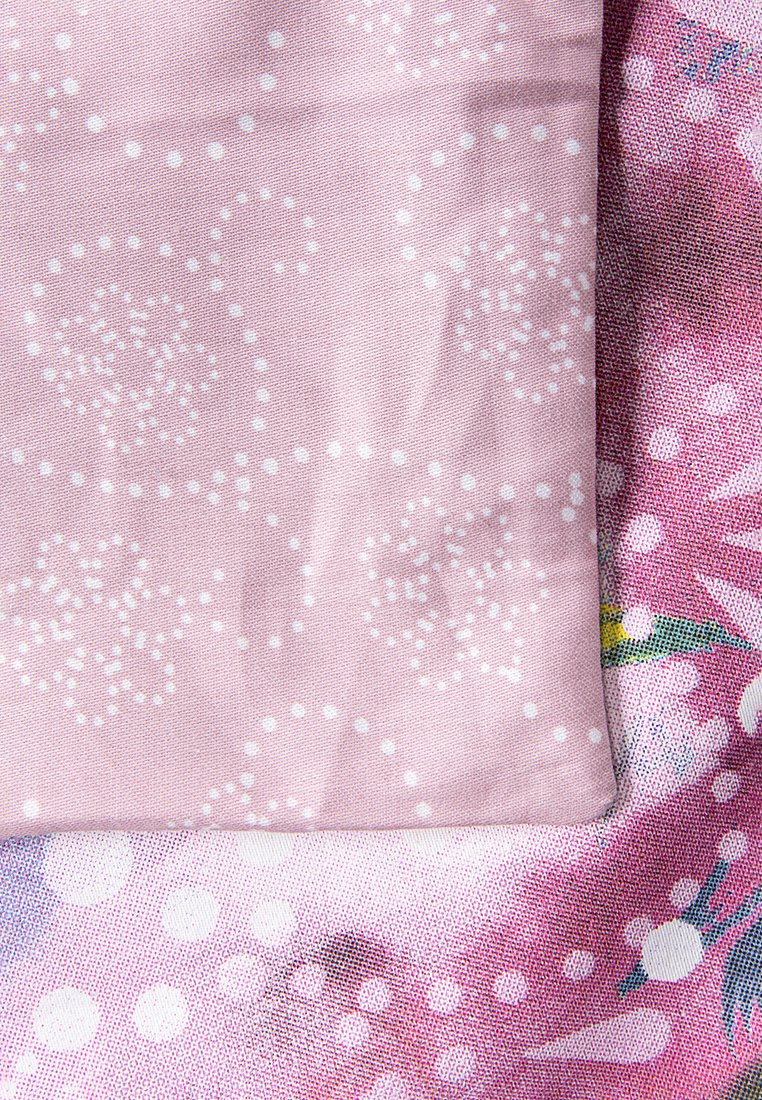 Helles rosa Stoff mit weißem Punktmuster, gefaltet über einem bunten blumigen Textil mit pinken und blauen Akzenten sowie unterschiedlichen Texturen.