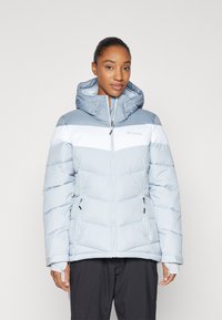 Giacca invernale blu gonfiabile con strisce orizzontali bianche, cappuccio, frontale con zip e tasche laterali; presenta una morbida texture trapuntata.