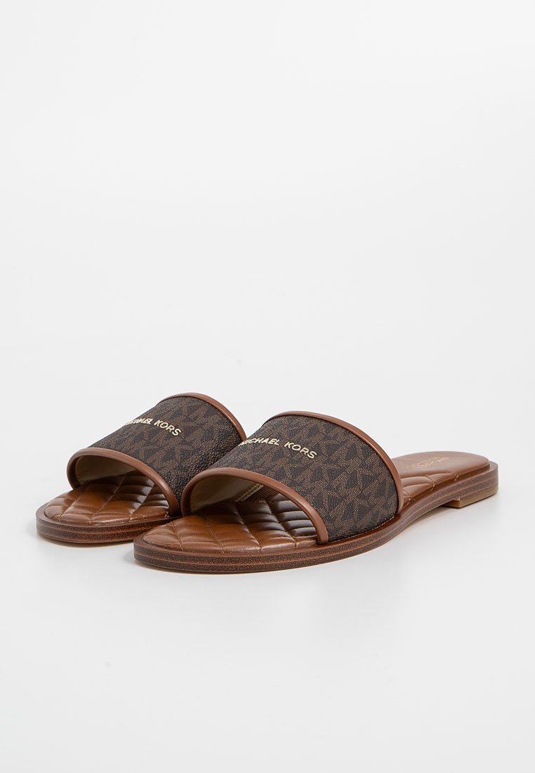 Sandalias deslizantes marrones con parte superior de textil con un patrón de monograma, plantilla acolchada y suela plana de goma. Acentos en oro con el logo.
