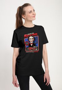 Czarny T-shirt z nadrukiem postaci w masce, czerwonymi spiralnymi akcentami oraz napisem "CHCĘ ZAGRAĆ W GRĘ."