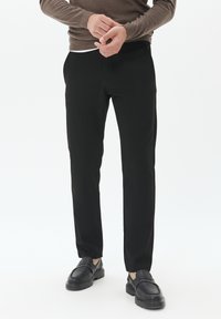 Pantalones negros ajustados con una textura suave, que presentan un corte clásico y bolsillos frontales, combinados con mocasines oscuros y un suéter en tonos neutros.