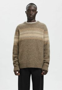 Pull rayé marron en matière douce avec poignets et ourlet côtelés, offrant une coupe décontractée et un col rond. Porté sur un top blanc.