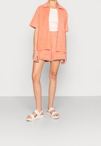 Chemise à manches courtes en éponge pêche et short assorti, associés à des sandales à plateforme crème. Texture lisse et coupe décontractée.