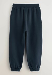 Pantalones de chándal azul marino fabricados con un tejido suave, que cuentan con una cinturilla elástica y puños fruncidos en los tobillos. Diseño minimalista, sin logotipos visibles.