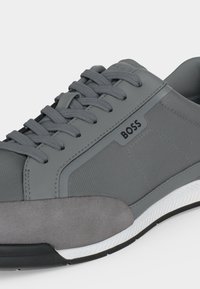 Baskets grises à lacets avec tige en tissu mixte et daim, semelle blanche et logo "BOSS" sur le panneau latéral.