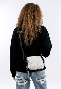 Borsa a tracolla grigia trapuntata con design strutturato, tracolla nera regolabile e superficie testurizzata. Indossata con jeans in denim strappati.