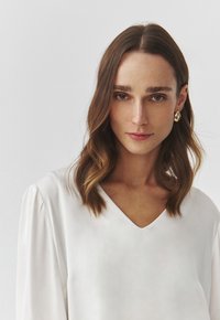 White, silky fabric blouse with a V-neck, soft draping, and puff sleeves. Features a smooth texture and a fitted silhouette.
