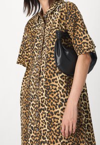 Kuvio leopardikankainen mekko, jossa on napitettava muotoilu pehmeästä kankaasta; sisältää lyhyet hihat ja väljän istuvuuden, yhdistettynä mustaan nahkalaukkuun.