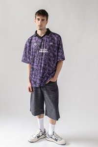 Violet raštuotas trumpomis rankovėmis džersis su juodu apykakle, su užrašu "MEILĖ MANO DRAMAI". Pora su tamsiai pilkais šortais ir baltais kojinėmis, sportbatiais.