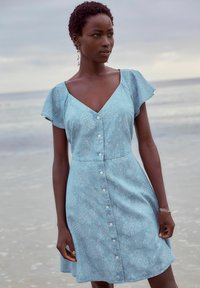 Vestido azul claro con mangas cortas y volantes, escote en V, cierre frontal con botones y patrón texturizado floral.