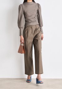 Graues, enges Oberteil mit Puffärmeln, beiget hohe Taillenhose, blaue Absatzsandalen und eine kleine braune Handtasche mit Griff.