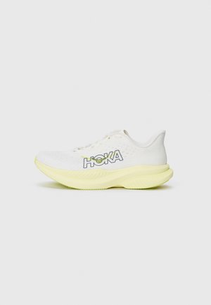 Weißer Sportschuh mit strukturiertem Obermaterial, hervorgehobenem HOKA-Logo und einem gelben Akzent an der dicken Sohle. Rundliche Zehenform und gepolsterte Passform.