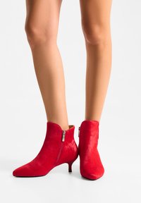 Rode enkellaarsjes gemaakt van zachte stof met een spitse neus en een kleine hak. Voorzien van een zijrits en een gladde textuur.