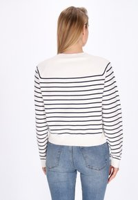 Weißer Pullover mit dunkelblauen horizontalen Streifen, gerippten Bündchen und Saum, rundem Ausschnitt und figurbetonter Passform, kombiniert mit hellblauen Jeans.
