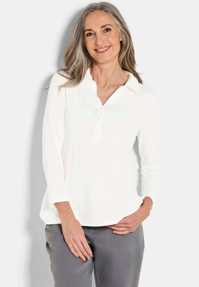 Witte blouse met lange mouwen, knoopsluiting en kraag, met verticale plooien en een gladde, zachte textuur. G gedragen met grijze broek.