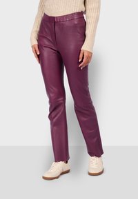 Pantalones de cuero morados con una textura suave y un diseño ajustado. Llevados con zapatillas de color claro, que cuentan con un cierre de cordones sencillo.